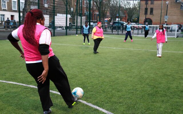 Girl kicking football on pitch