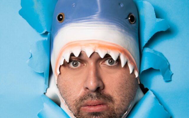 Man with shark head poking through blue screen