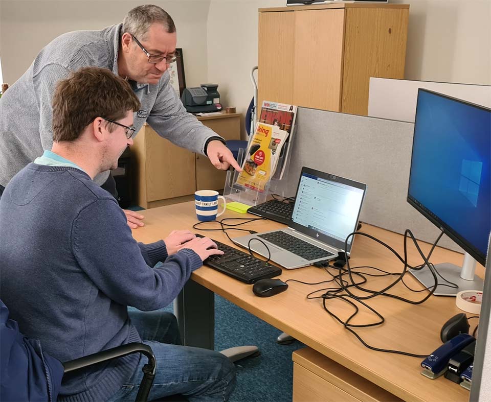 Younger man at laptop with older man helping